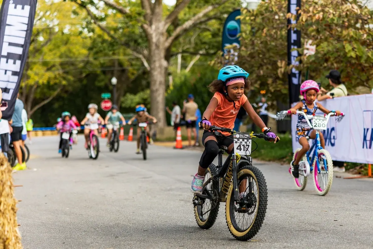 Young racers with number plates riding down a course lined with spectators