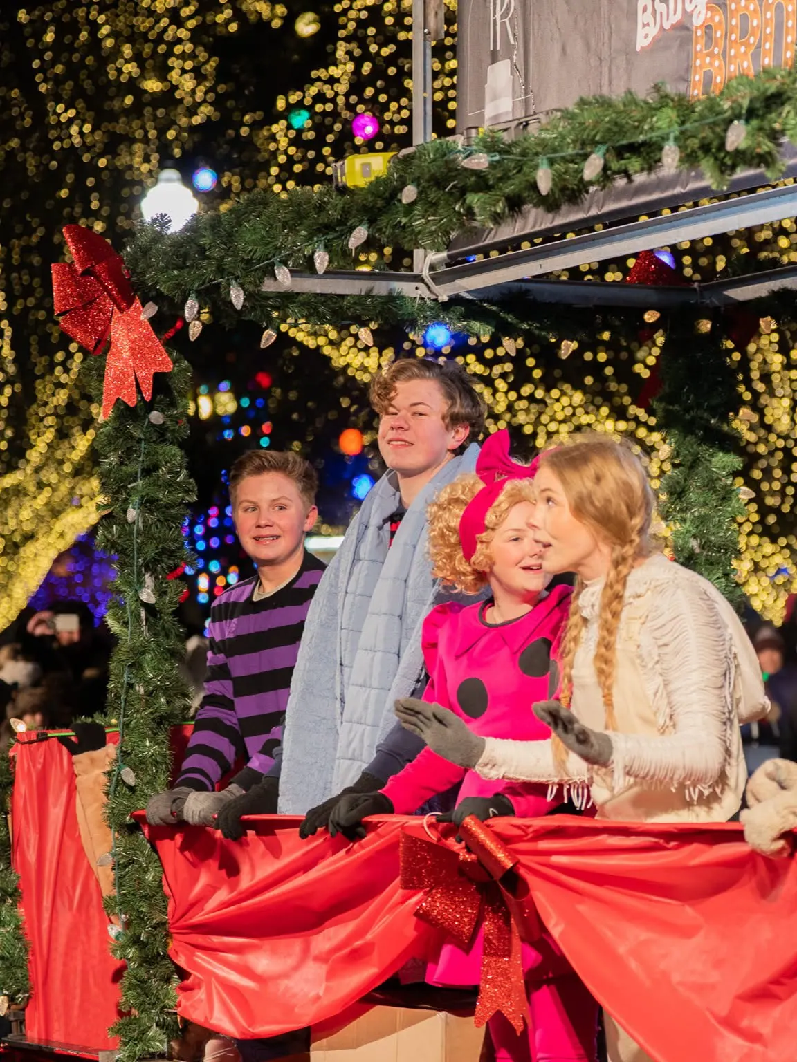Performers in holiday costumes on a decorated stage under Christmas lights