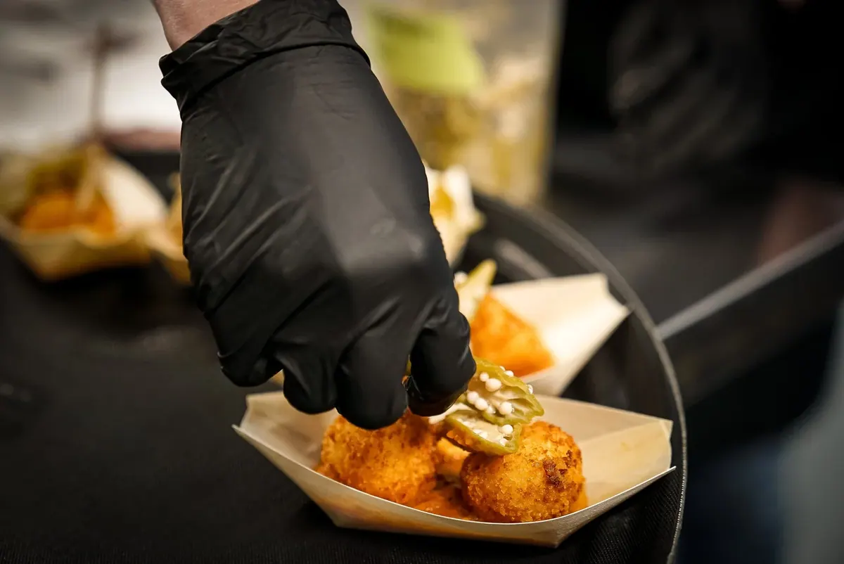 Gloved hand garnishing a fried bite in a paper boat